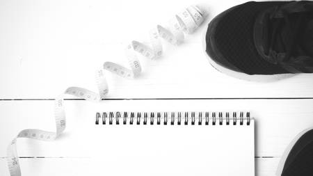 running shoes with notebook and measuring tape on white wood table black and white tone color styleの写真素材
