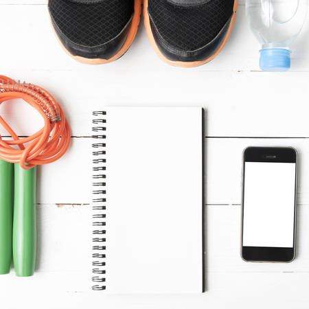 fitness equipment : running shoes,jumping rope,drinking water,notebook and phone on white wood tableの写真素材
