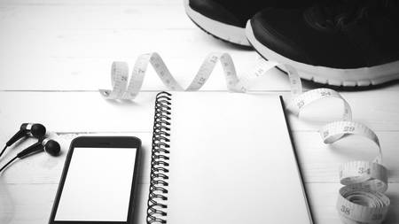 running shoes,measuring tape,notebook and phone on white wood table black and white tone color styleの写真素材