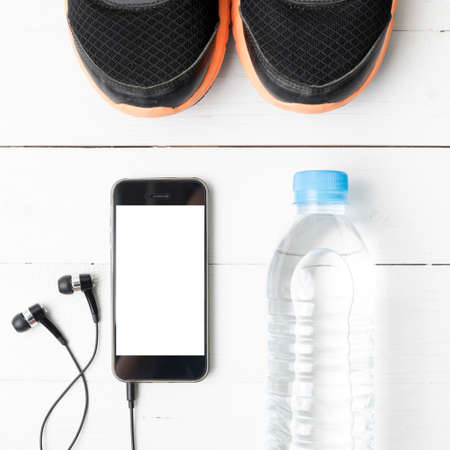 fitness equipment : running shoes,drinking water and phone on white wood table