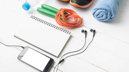 fitness equipment : running shoes,towel,jumping rope,water bottle,phone and notepad on white wood...
