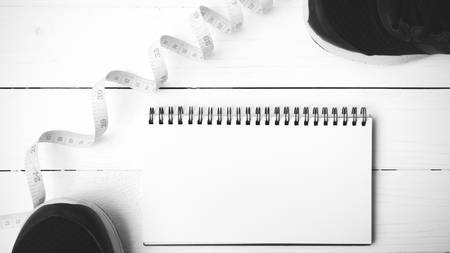 running shoes with notebook and measuring tape on white wood table black and white tone color styleの写真素材