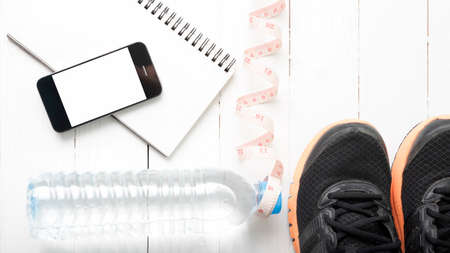 running shoes,measuring tape,drinking water,notebook and phone on white wood tableの写真素材