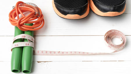 fitness equipment : running shoes,jumping rope and measuring tape on white wood tableの写真素材