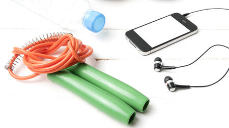 fitness equipment : running shoes,jumping rope,phone and water bottle on white wood table
