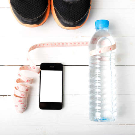 fitness equipment : running shoes,drinking water,measuring tape and phone on white wood tableの写真素材