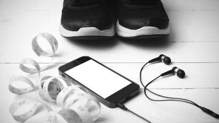 running shoes,measuring tape and phone on white wood table black and white tone color styleの写真素材
