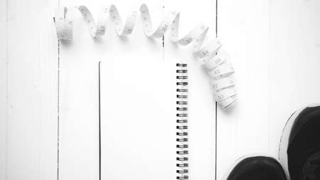 running shoes with notebook and measuring tape on white wood table black and white tone color styleの写真素材