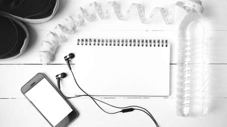running shoes,measuring tape,drinking water,notebook and phone on white wood table black and white tone color styleの写真素材