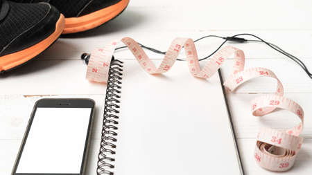 running shoes,measuring tape,notebook and phone on white wood table