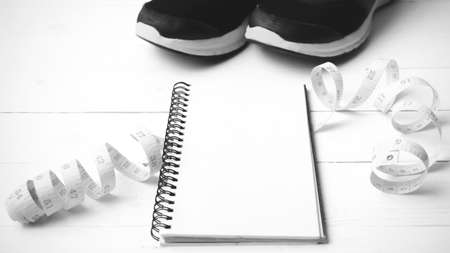 running shoes with notebook and measuring tape on white wood table black and white tone color styleの写真素材