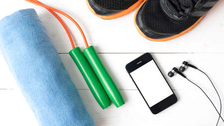fitness equipment : running shoes,towel,jumping rope and phone on white wood tableの写真素材
