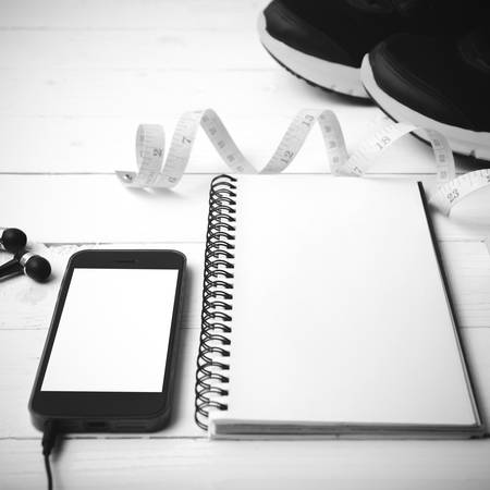running shoes,measuring tape,notebook and phone on white wood table black and white tone color style