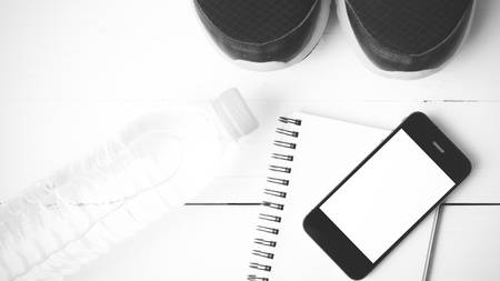 fitness equipment : running shoes,drinking water,notebook and phone on white wood table black and white tone color styleの写真素材
