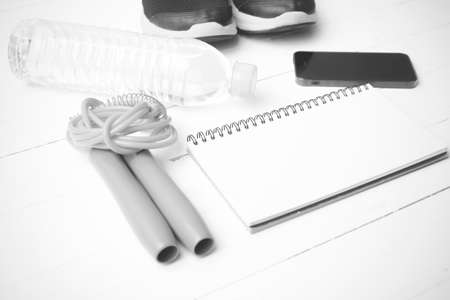 fitness equipment : running shoes,jumping rope,drinking water,notebook and phone on white wood table black and white tone color styleの写真素材
