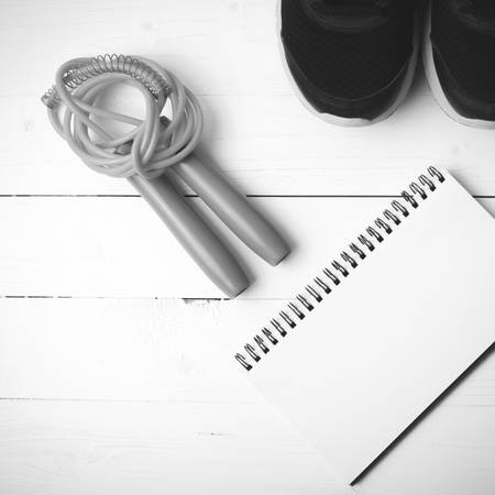 fitness equipment : running shoes,jumping rope and notepad on white wood table black and white color tone styleの写真素材