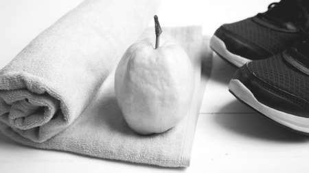 fitness equipment : running shoes,towel and guava fruit on white wood table black and white color...