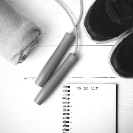 fitness equipment : running shoes,towel,jumping rope and notebook write to do list on white wood...