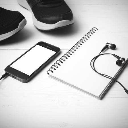 running shoes,notebook and phone on white wood table black and white tone color styleの写真素材