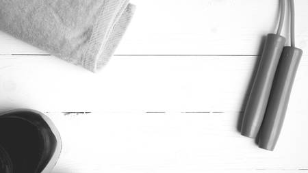 fitness equipment: towel,jumping rope and running shoes on white wood table black and white color...