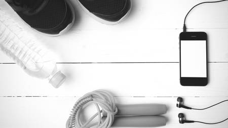 fitness equipment : running shoes,jumping rope,phone and water bottle on white wood table black and white color tone styleの写真素材