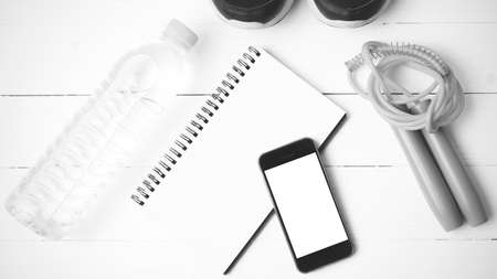 fitness equipment : running shoes,jumping rope,drinking water,notebook and phone on white wood table...