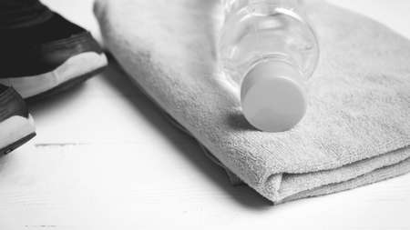 fitness equipment: towel,drinking water and running shoes on white wood table black and white color styleの写真素材