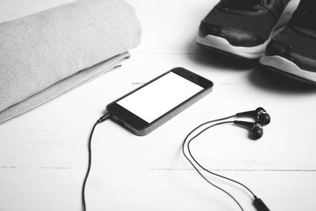 fitness equipment:running shoes,towel and smart phone on white wood table black and white color...