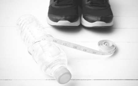 fitness equipment : running shoes,drinking water and measuring tape on white wood table black and white tone color styleの写真素材