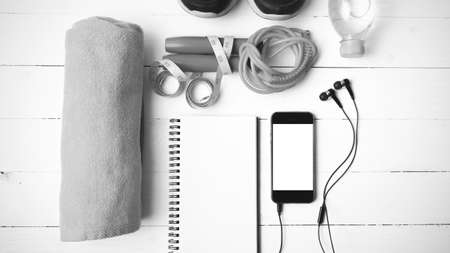 fitness equipment : running shoes,towel,jumping rope,water bottle,phone,notepad and measuring tape on white wood table black and white color tone styleの写真素材