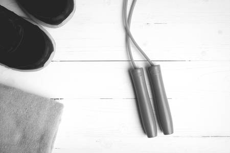 fitness equipment: towel,jumping rope and running shoes on white wood table black and white color...