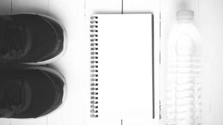 fitness equipment : running shoes,drinking water and notebook on white wood table black and white tone color styleの写真素材