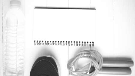 fitness equipment : running shoes,jumping rope,drinking water and notepad on white wood table  black and white tone color styleの写真素材