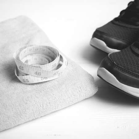 fitness equipment : running shoes,towel and measuring tape on white wood table black and white color styleの写真素材