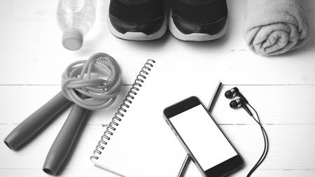 fitness equipment : running shoes,towel,jumping rope,water bottle,phone and notepad on white wood table black and white color tone styleの写真素材