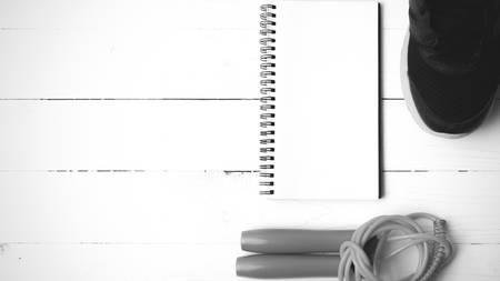 fitness equipment : running shoes,jumping rope and notepad on white wood table black and white color...