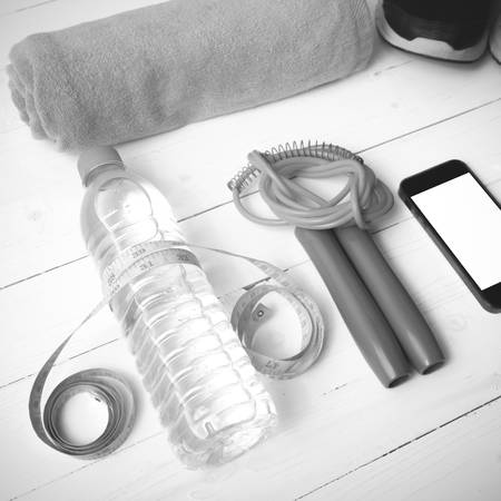 fitness equipment : running shoes,towel,jumping rope,water bottle,phone and measuring tape on white wood table black and white color tone styleの写真素材