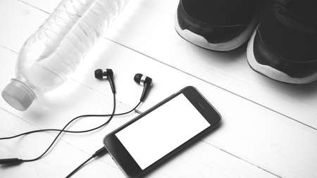 fitness equipment : running shoes,drinking water and phone on white wood table black and white tone color styleの写真素材