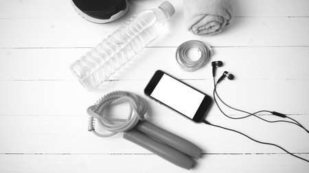 fitness equipment : running shoes,towel,jumping rope,water bottle,phone and measuring tape on white wood table black and white color tone styleの写真素材