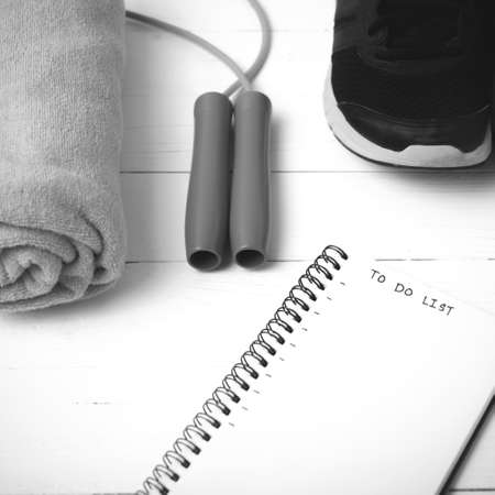 fitness equipment : running shoes,towel,jumping rope and notebook write to do list on white wood table black and white color tone styleの写真素材