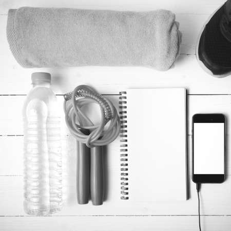 fitness equipment : running shoes,towel,jumping rope,water bottle,phone and notepad on white wood...