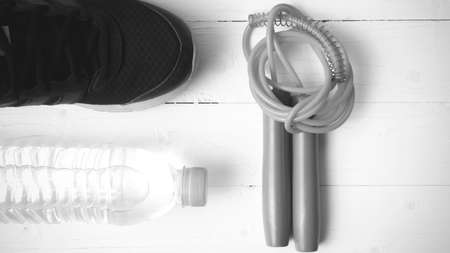 fitness equipment : running shoes,jumping rope and water bottle on white wood table black and white color tone styleの写真素材