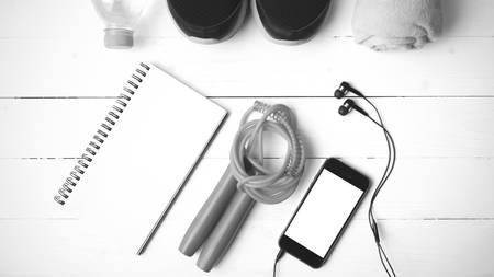 fitness equipment : running shoes,towel,jumping rope,water bottle,phone and notepad on white wood table black and white color tone styleの写真素材