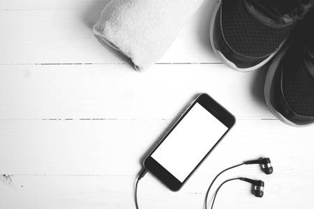 fitness equipment:running shoes,towel and smart phone on white wood table black and white color...