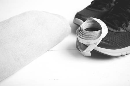 fitness equipment : running shoes,towel and measuring tape on white wood table black and white color styleの写真素材