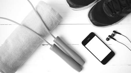 fitness equipment : running shoes,towel,jumping rope and phone on white wood table black and white color tone styleの写真素材