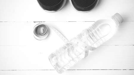 fitness equipment : running shoes,drinking water and measuring tape on white wood table black and white tone color styleの写真素材