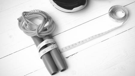 fitness equipment : running shoes,jumping rope and measuring tape on white wood table black and white color tone styleの写真素材