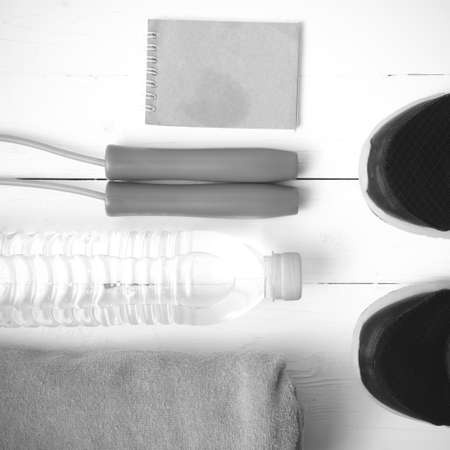fitness equipment : running shoes,towel,jumping rope,water bottle and notepad on white wood table black and white color tone styleの写真素材