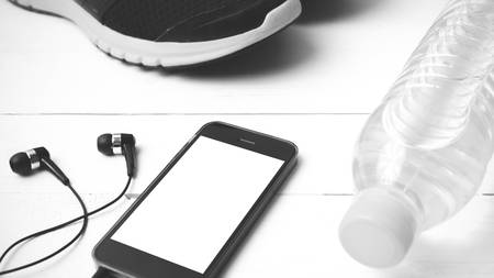 fitness equipment : running shoes,drinking water and phone on white wood table black and white tone color styleの写真素材